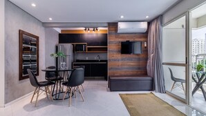 Eine moderne Küche mit dunklen Schränken, einer Mikrowelle und einem eingebauten Backofen. Es gibt einen Essbereich mit Tisch und Stühlen sowie ein großes Fenster mit Vorhängen.