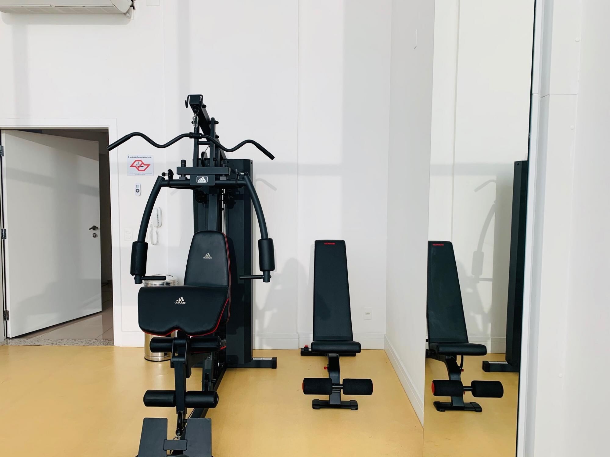 A gym with a bench press, a leg press machine, and a wall-mounted exercise station.