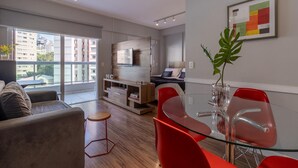 Un salon moderne avec une table à manger en verre, des chaises rouges, un canapé et un téléviseur fixé à un mur en bois.