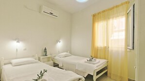 A hotel room with two beds, a bedside table with a lamp, an air conditioning unit, and a window with yellow curtains. - Jasmin in Katavolos With 1 Bedrooms and 1 Bathrooms (Corfu)