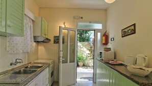 A narrow kitchen with a sink, stove, and a door leading to a garden. - Jasmin in Katavolos With 1 Bedrooms and 1 Bathrooms (Corfu)
