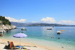 A beach with clear water, boats, and a mountainous backdrop.