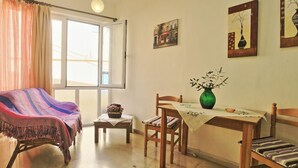 A cozy living room with a striped armchair, a wooden dining table with chairs, a small side table with a vase, and a window with curtains. - Jasmin in Katavolos With 1 Bedrooms and 1 Bathrooms (Corfu)