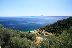 A coastal view with a beach, a small cluster of buildings, and dense greenery.