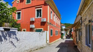 Eine schmale Straße mit einem roten Gebäude auf der linken Seite und einem Steinhaus auf der rechten Seite.