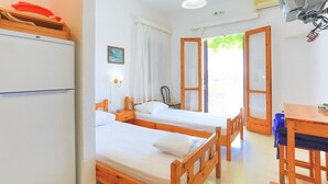 Ein Zimmer mit zwei Holzbetten, einem Schreibtisch und einem Stuhl. Es gibt ein Fenster mit Vorhängen, eine Wand-Klimaanlage und eine Deckenleuchte.