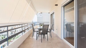 Un balcón con una mesa, sillas, un ventanal de vidrio y vista a la ciudad.