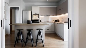 Una cocina moderna con una isla central, taburetes de bar, microondas, estufa y refrigerador.