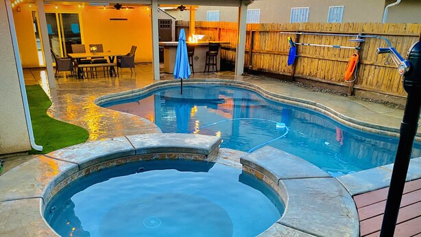 Ein Schwimmbecken mit Whirlpool, umgeben von einer Holzterrasse und einer Terrasse mit Gartenmöbeln.