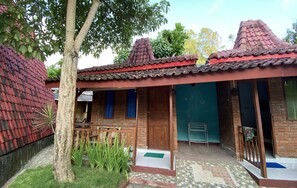 A traditional house with a tiled roof, a wooden door, and a small porch area. - Kayu Watu Cottage Gunung Kidul (Tepus)