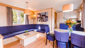 Een moderne woonkamer met een blauwe bank, een houten salontafel en een eetgedeelte met blauwe stoelen.