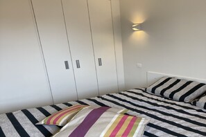 Un dormitorio con cama, ropa de cama a rayas, un armario y una lámpara de pared.