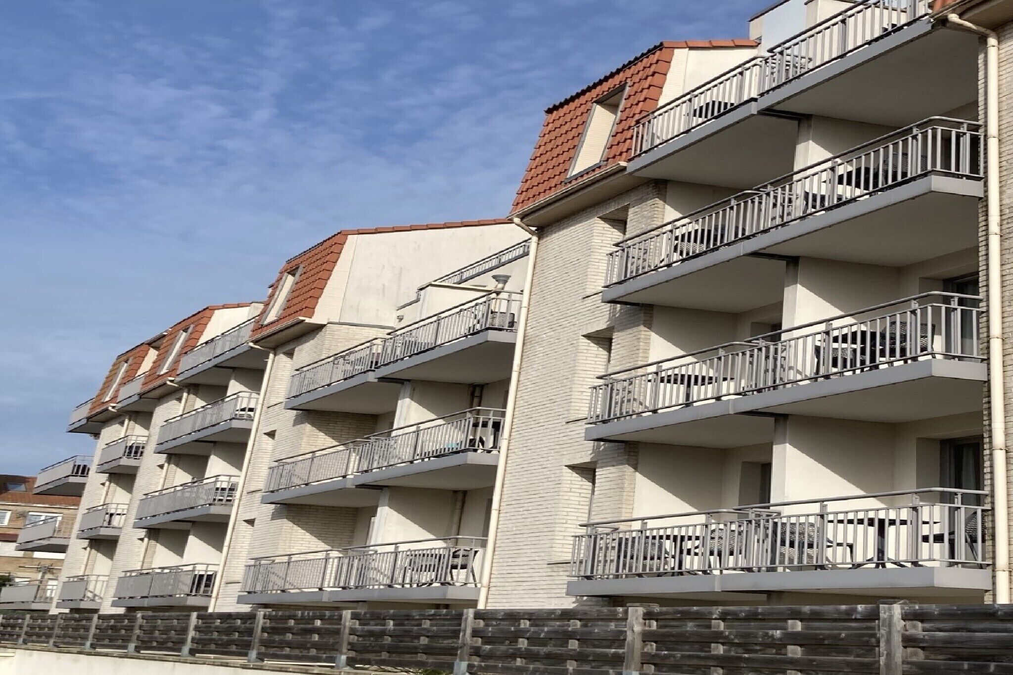Un immeuble résidentiel à plusieurs étages, doté de balcons et d’une façade en briques, avec un ciel dégagé.