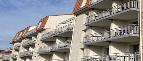 Un immeuble résidentiel à plusieurs étages, doté de balcons et d’une façade en briques, avec un ciel dégagé.