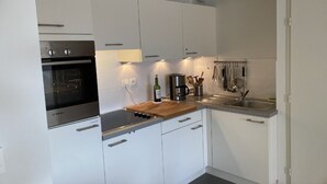 Moderni keittiö, jossa on valkoiset kaapit, Bosch-uuni, puinen työtaso ja kahvinkeitin.