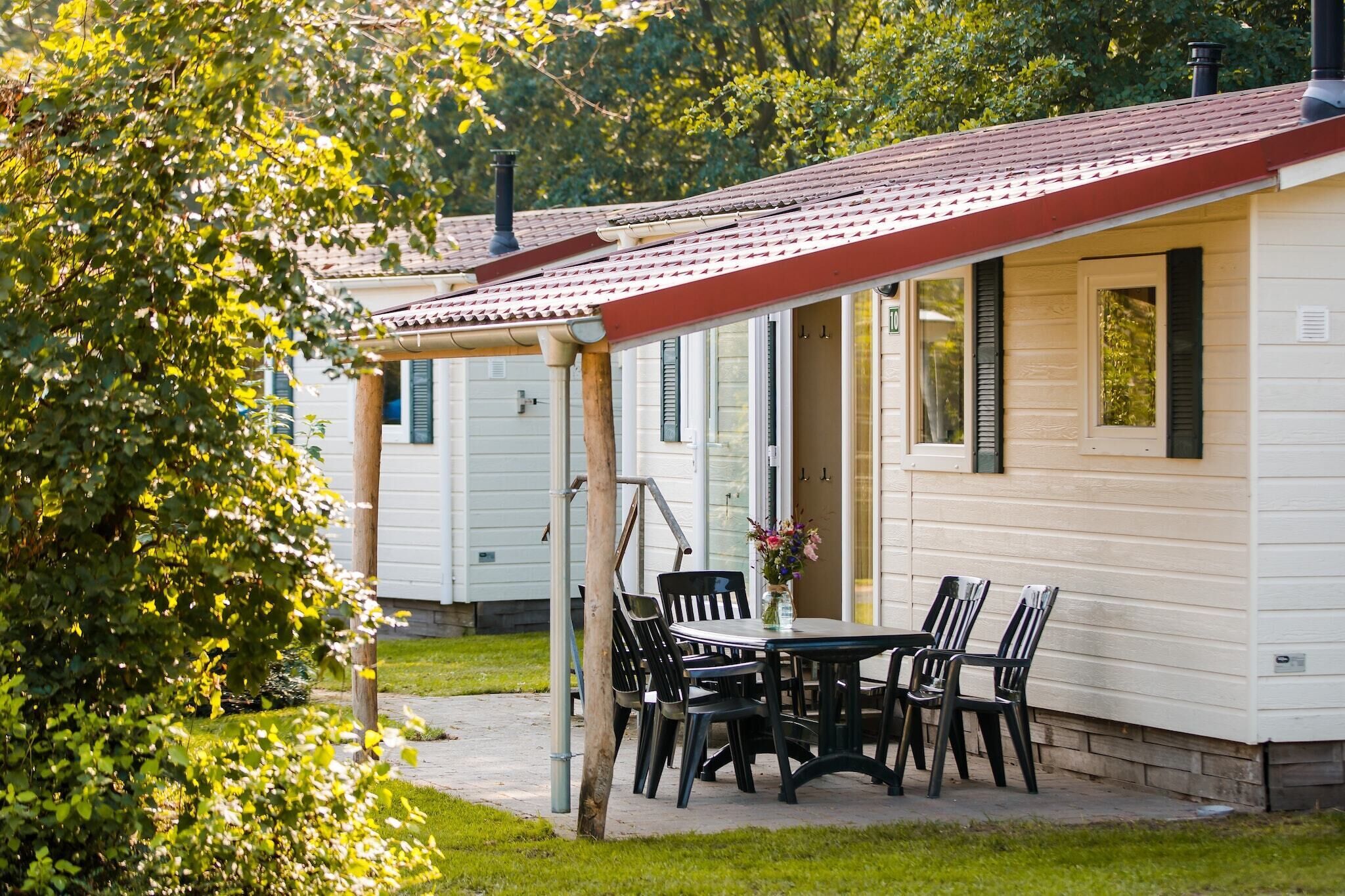 A mobile home with a covered patio area, a table with chairs, and a potted plant.