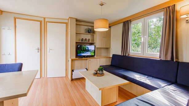 Un espacio habitable compacto con sofá, televisor, mesa de comedor y ventana con cortinas.