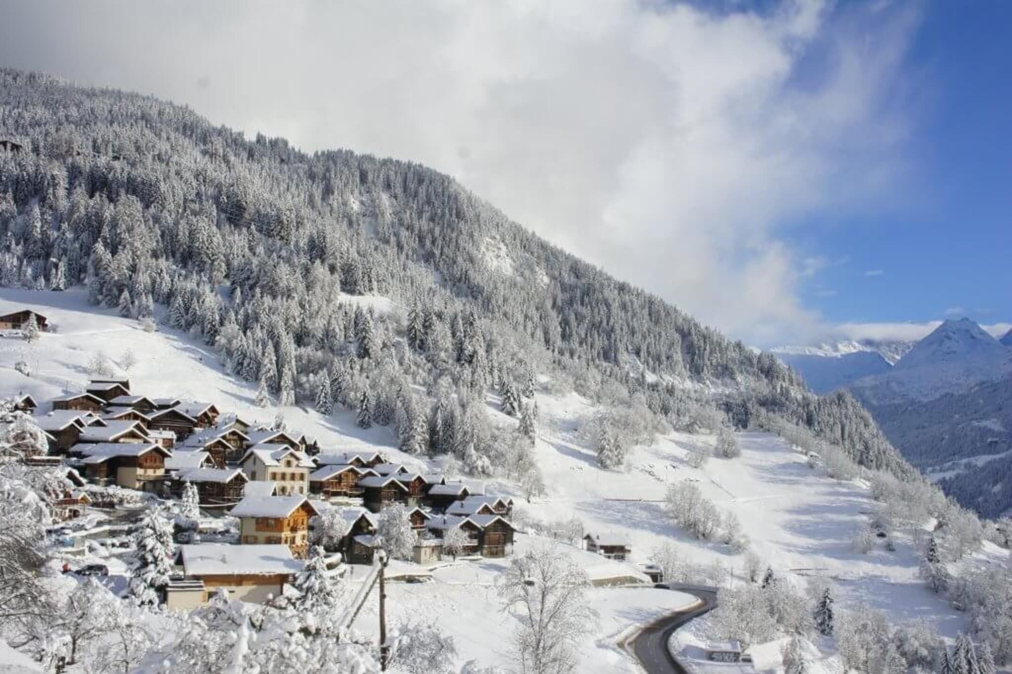 A snow-covered village with wooden chalets, a winding road, and a mountain backdrop.
