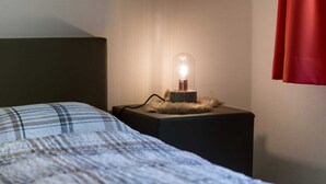 Een bed met een geruite deken, een bedlamp met een glazen voet, en een bont plaid op een nachtkastje.