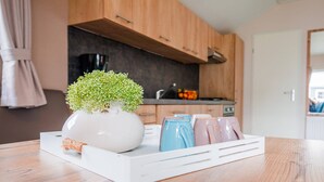 A kitchen with wooden cabinets, a white tray with a vase of green plants, and ceramic mugs. - Covered Terrace Chalet at Leukermeer (Well)