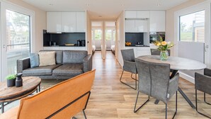 Une cuisine moderne avec des meubles blancs, un îlot central et un coin repas comprenant des chaises grises et une table ronde.