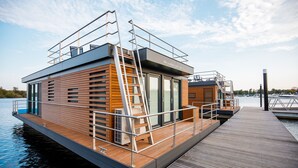 Une maison flottante dotée d’une terrasse en bois, d’une échelle et d’une porte en verre.