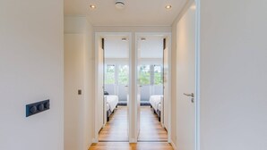 Un couloir avec une porte double donnant sur une chambre à coucher équipée d’un lit et d’une fenêtre.
