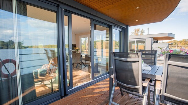 Une terrasse extérieure moderne, dotée de portes vitrées donnant sur un espace repas et offrant une vue sur un plan d’eau.
