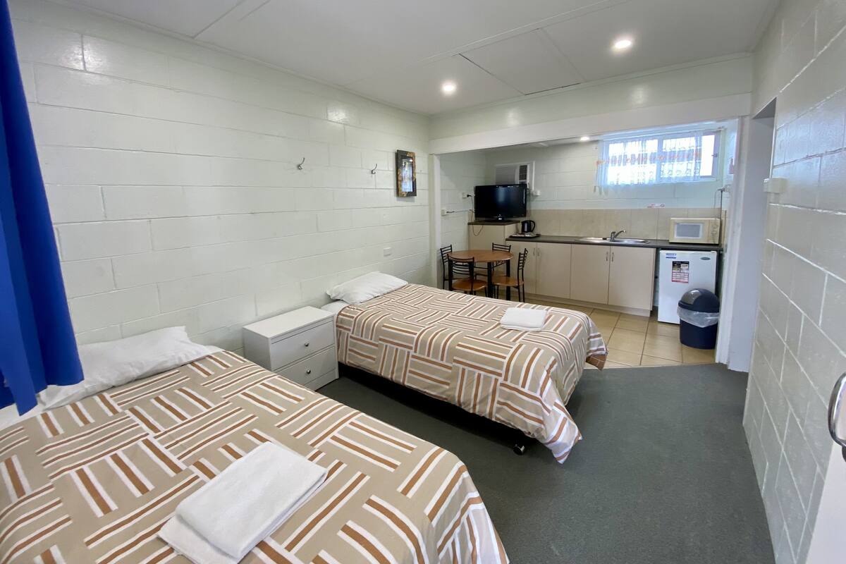 Une chambre de taille modeste, équipée de deux lits, d’une petite kitchenette, d’un téléviseur et d’une fenêtre avec des rideaux.
