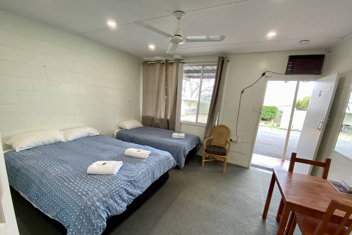 Une chambre avec deux lits, une chaise, une table et un ventilateur de plafond.