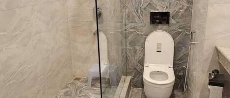 A modern bathroom with a glass-enclosed shower, a toilet, and a hand soap dispenser.