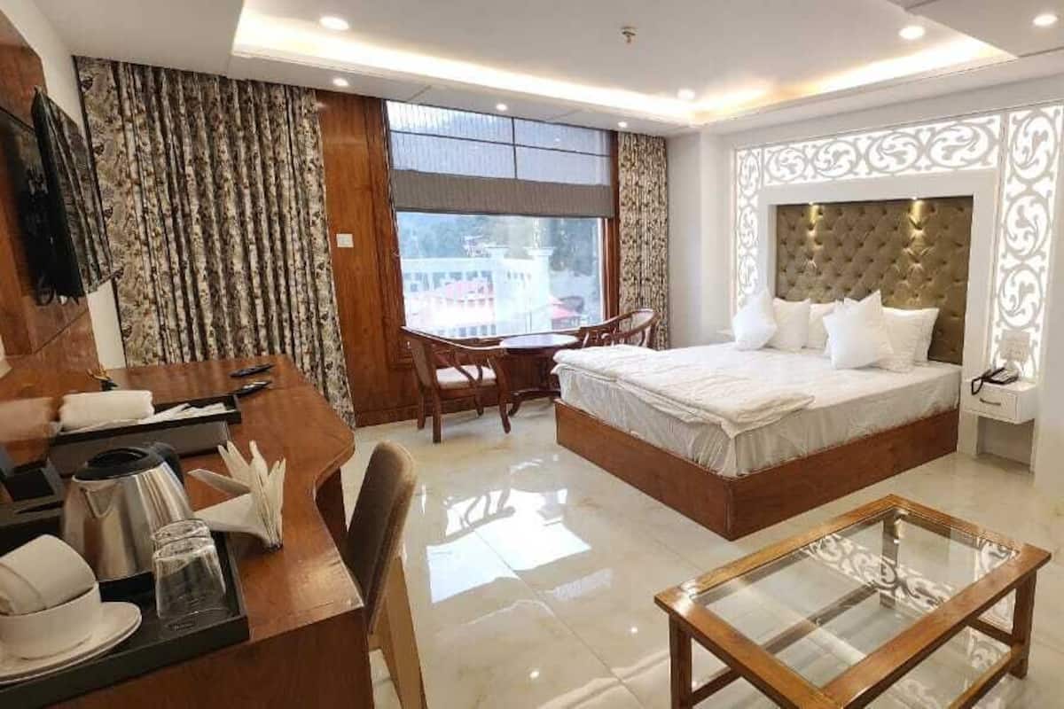 A hotel room with a large bed, a desk with a chair, a small table, and a sofa.