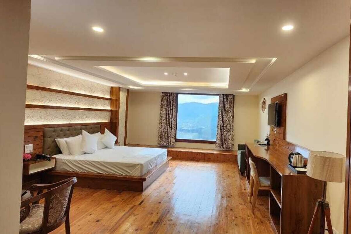 A hotel room with a bed, desk, chair, and a large window with a view.