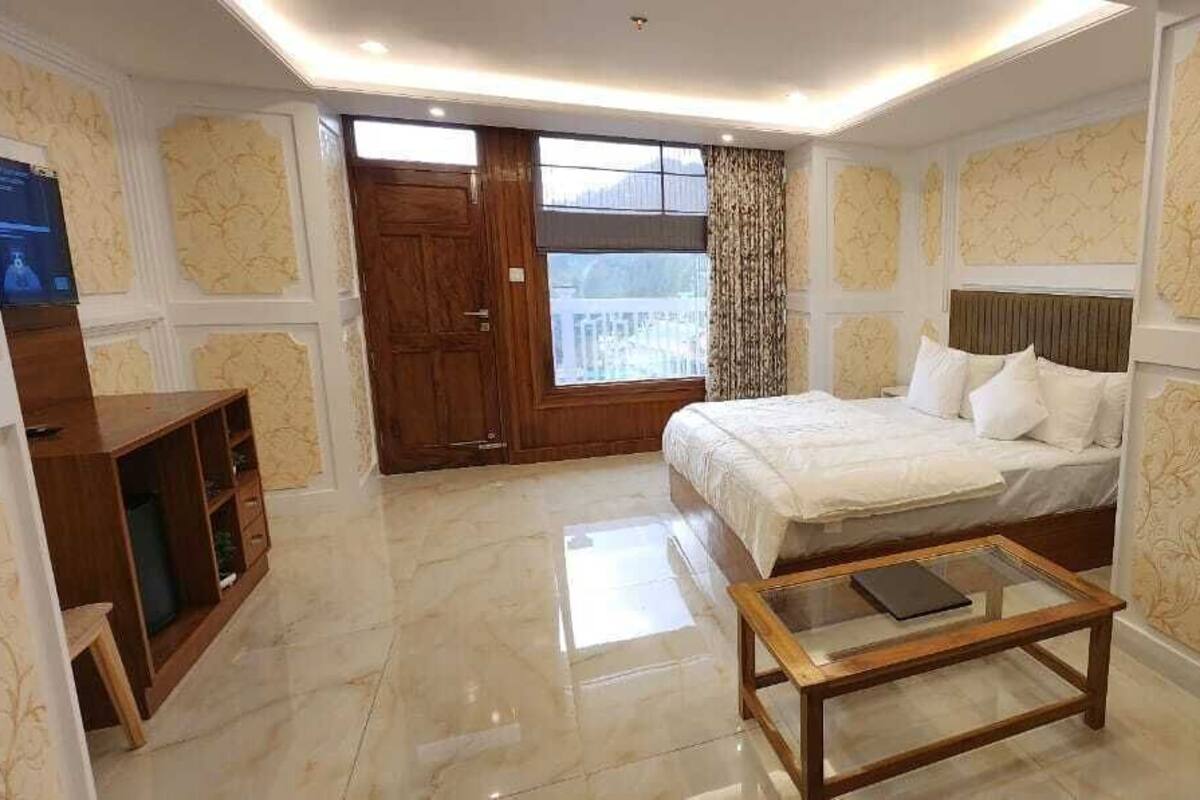 A bedroom with a bed, a wooden nightstand, a glass-top coffee table, and a large window.
