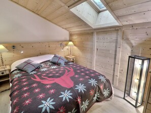 A bedroom with a skylight, wooden walls, a bed with floral bedding, bedside lamps, and a nightstand.