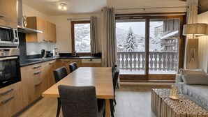 Una cocina moderna con comedor, suelo de madera y vistas a un paisaje nevado a través de grandes ventanales.