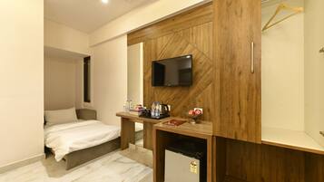 Un dormitorio con cama, escritorio con televisor, refrigerador pequeño y armario de madera.