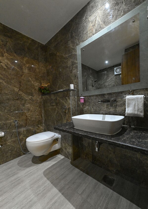 A modern bathroom with a marble wall, a white toilet, a large sink, and a mirror.