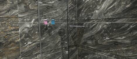 Un baño moderno con cabina de ducha de vidrio, paredes de mármol y un inodoro con toallero.