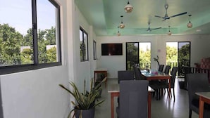 Un vaste espace dédié à la salle à manger, avec une grande table et des chaises, une plante en pot et un téléviseur fixé au mur.