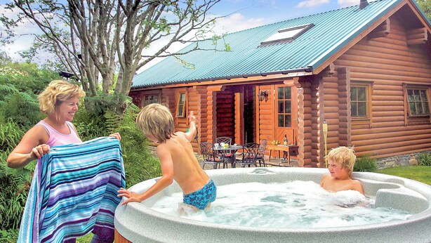 Een vakantiehuisje van hout met een bubbelbad, een eethoek en een terras.
