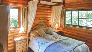 Een slaapkamer in een houten hutje, met een bed, nachtkastjes, een dressoir en een raam met gordijnen.