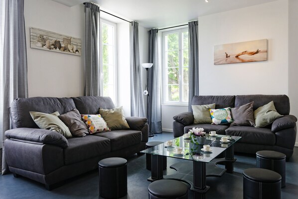 A modern living room with two dark sofas, a glass coffee table, and a large window with curtains.