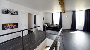 Ein geräumiger Wohnbereich mit hoher Decke, dunklem Holzboden, einer Treppe und einer Sofagarnitur.
