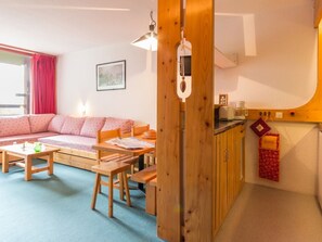Ein gemütliches Wohnzimmer mit einer Couch, einem Holztisch und einer Küchenzeile mit Schränken und einer hängenden Kochutensilienstange.