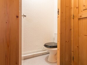 A wooden door leading to a bathroom with a white toilet and a visible pipe on the wall.