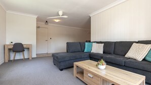 En moderne stue med en grå hjørnesofa, et træ sofabord og et skrivebord med en stol.