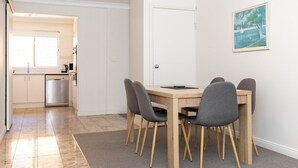 Et moderne køkken med hvide skabe, en rustfri opvaskemaskine og et træspisebord med fire grå stole.