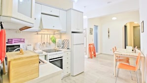 Una cocina moderna con armarios blancos, encimera de madera y comedor con sillas anaranjadas.
