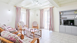 Una sala de estar con muebles de mimbre, cortinas a rayas y un televisor sobre un mueble.